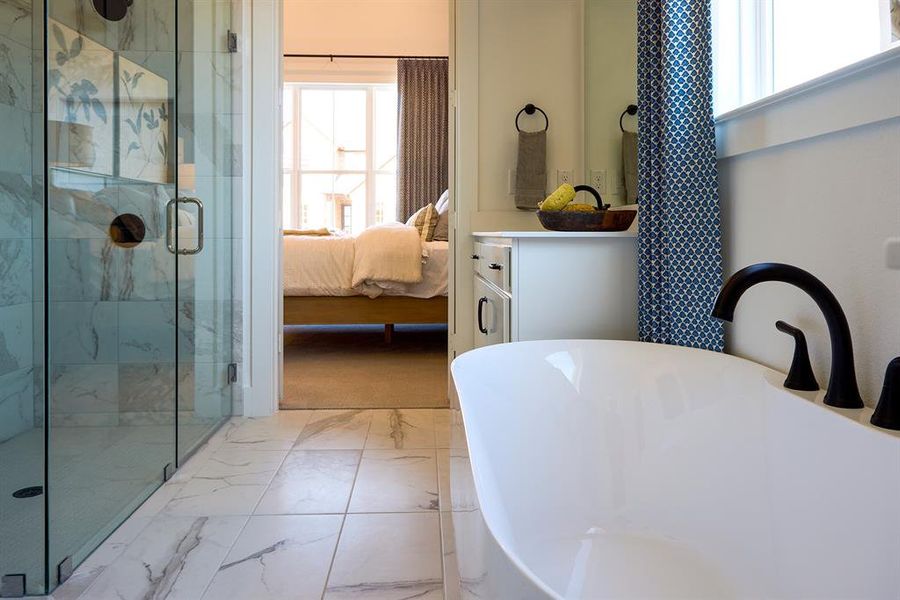 Bathroom featuring light marble finish flooring, a marble finish shower, vanity, a freestanding bath, and ensuite bathroom