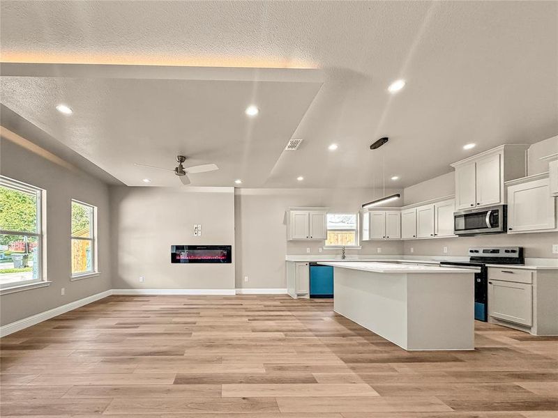 Open-concept living space featuring wood-finish flooring, recessed lighting, and an electric fireplace Open-concept living space featuring wood-finish flooring, recessed lighting, and an electric fireplace