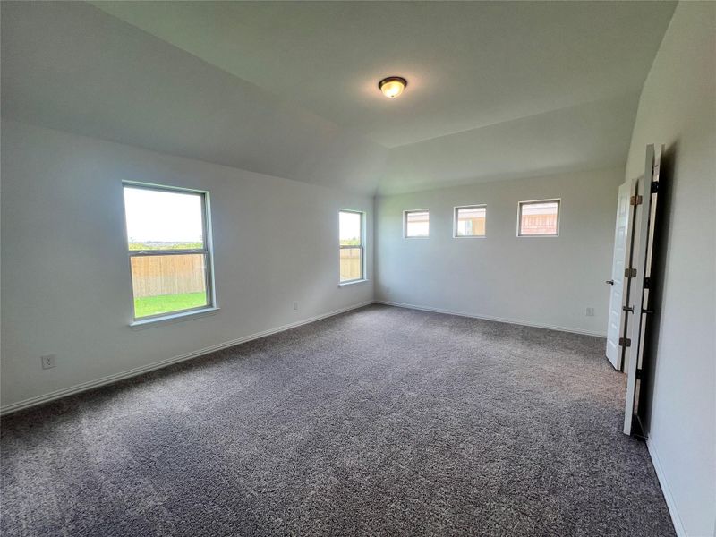 Spare room featuring dark colored carpet and lofted ceiling