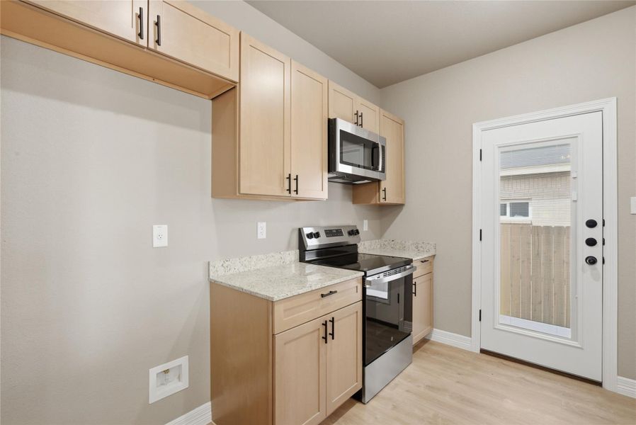 Kitchen featuring light wood finish cabinets, stainless steel appliances, light stone countertops, and light wood finished floors