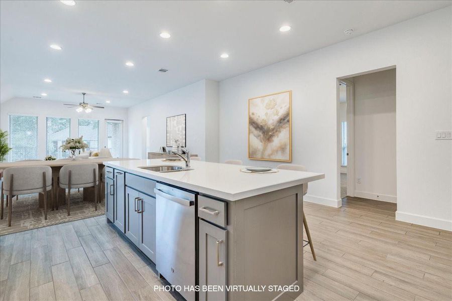 The kitchen features a large island with a sink and a built-in dishwasher, complemented by light-colored countertops and cabinetry