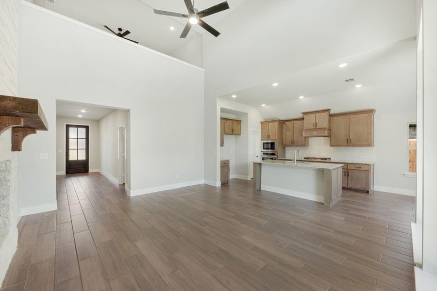 Open-concept living area with high ceilings, wood-look floors, and kitchen with island and light wood cabinets Open-concept living area with high ceilings, wood-look floors, and kitchen with island and light wood cabinets