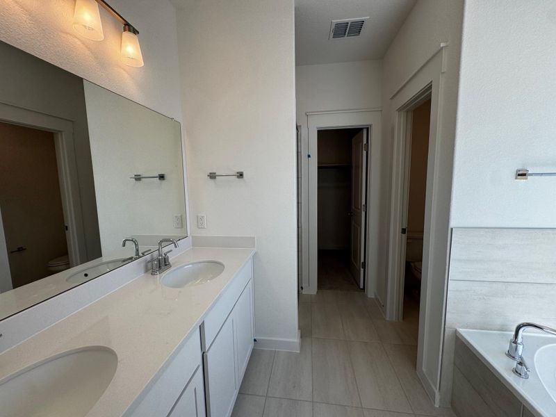 Full bathroom featuring double vanity, a garden tub, a walk in closet, and light tile patterned floors Full bathroom featuring double vanity, a garden tub, a walk in closet, and light tile patterned floors