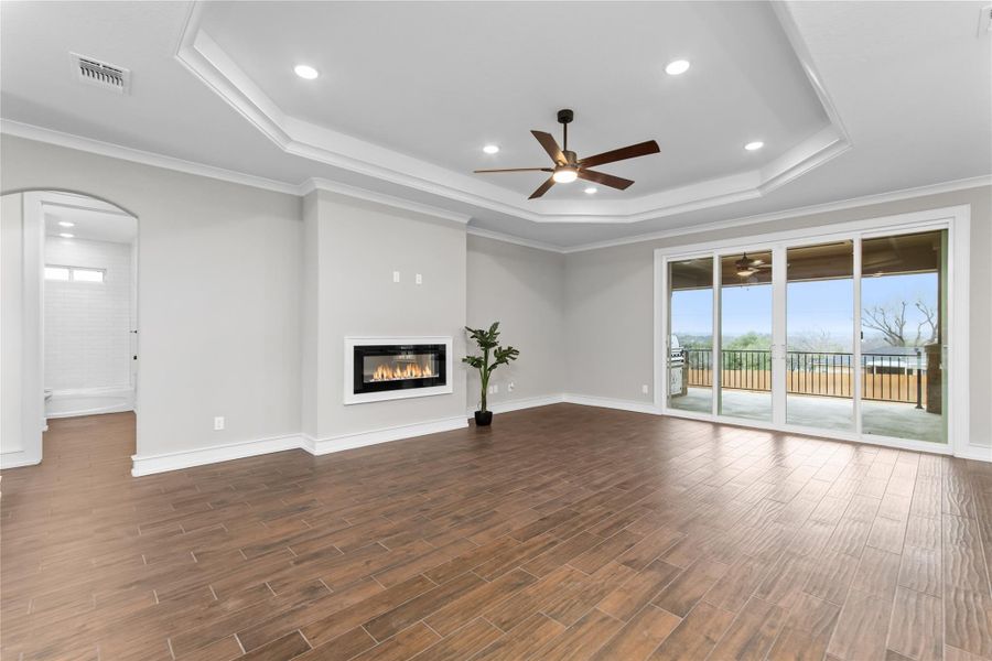 Unfurnished living room with a tray ceiling, ceiling fan, a glass covered fireplace, arched walkways, and dark wood-style flooring Unfurnished living room with a tray ceiling, ceiling fan, a glass covered fireplace, arched walkways, and dark wood-style flooring