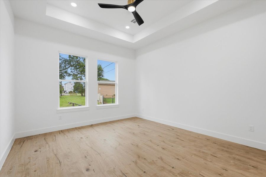Your Private Retreat. Escape to comfort in this spacious primary bedroom featuring a deep tray ceiling accent, a contemporary black ceiling fan, and large twin windows that fill the room with soothing natural light.