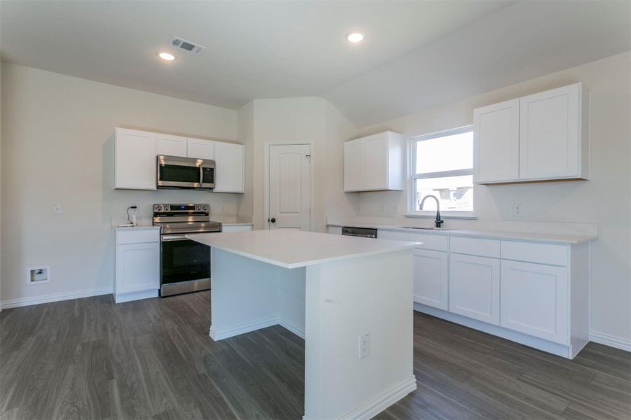 Kitchen with visible vents, a kitchen island, dark wood-style floors, and appliances with stainless steel finishes Kitchen with visible vents, a kitchen island, dark wood-style floors, and appliances with stainless steel finishes