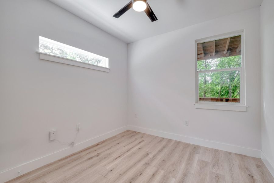 A quiet bedroom featuring light-toned flooring and two distinct windows inviting natural light. A quiet bedroom featuring light-toned flooring and two distinct windows inviting natural light.