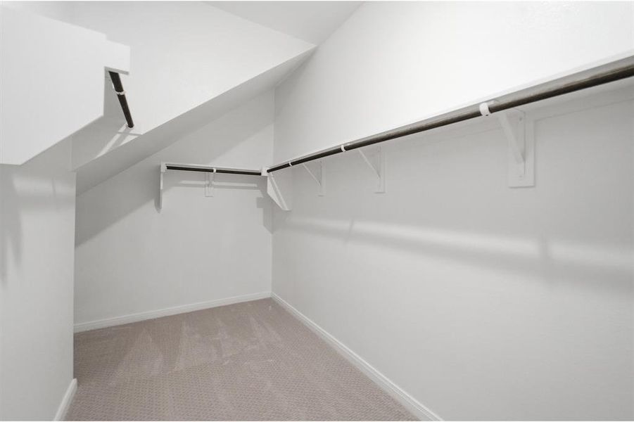 Walk-in closet with sloped ceilings, white walls, and light-colored carpeting