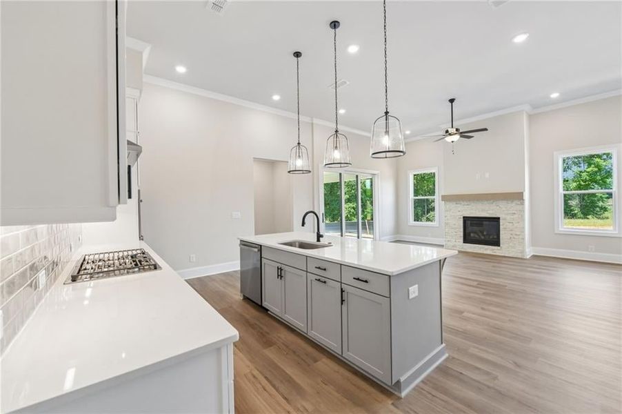 Gourmet kitchen with white countertops and a gas cooktop, featuring a central island with a sink and pendant lighting