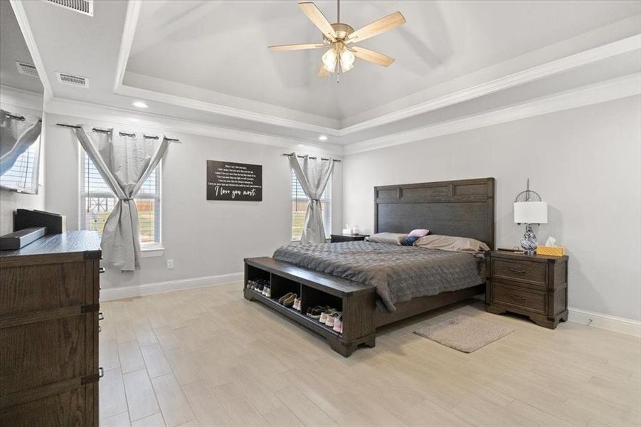 Bedroom with baseboards, a raised ceiling, visible vents, and light wood-style floors