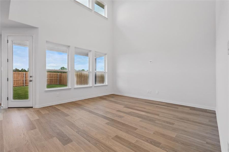 Unfurnished living room with light wood-style flooring, baseboards, and a towering ceiling Unfurnished living room with light wood-style flooring, baseboards, and a towering ceiling