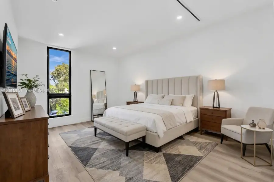 Neutral interior space featuring wood-finish flooring, recessed lighting, and a tall vertical window with a dark frame Neutral interior space featuring wood-finish flooring, recessed lighting, and a tall vertical window with a dark frame