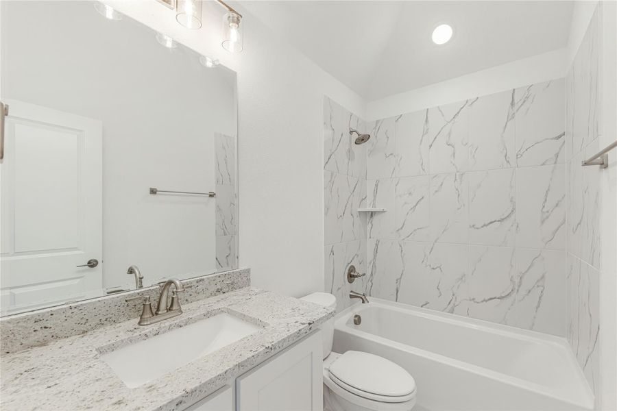 Bathroom with granite countertop vanity, white tub, and marble-style tile shower surround Bathroom with granite countertop vanity, white tub, and marble-style tile shower surround