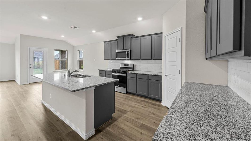 Modern kitchen featuring granite countertops, dark gray cabinetry, stainless steel appliances, a subway tile backsplash, and wood-finish flooring