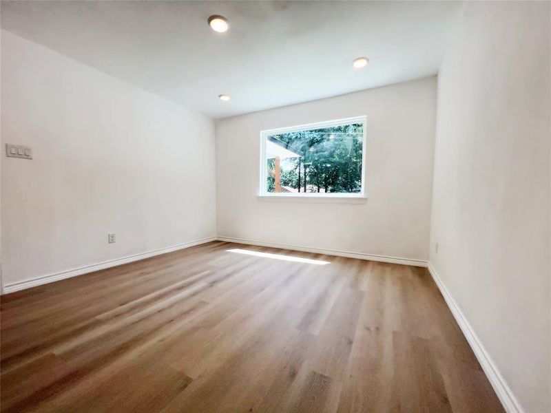 Spacious room featuring wood-finish flooring, recessed lighting, and a large window with white trim