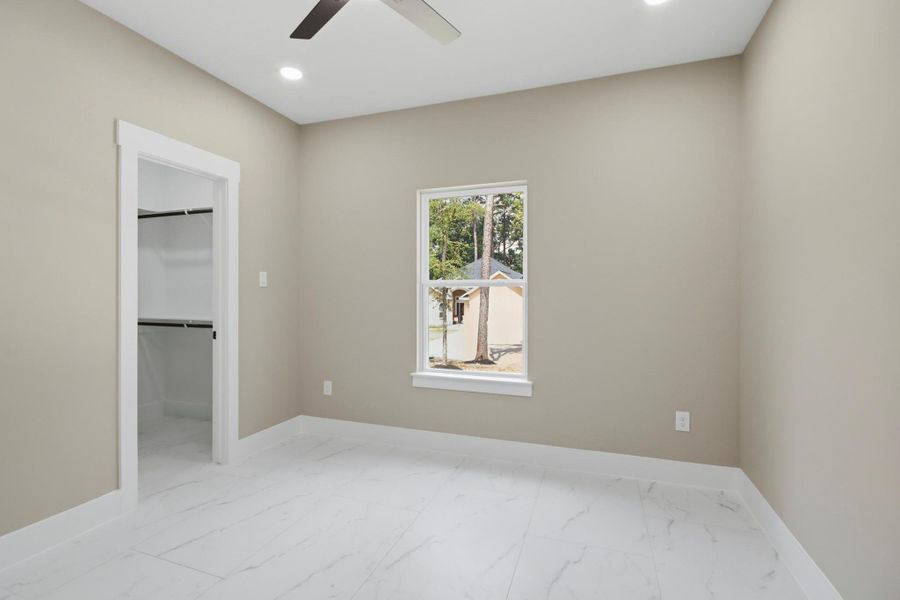 This bright bedroom features premium tile flooring, a large single-hung window framing backyard views, high ceilings with recessed lighting, and a spacious walk-in closet. This bright bedroom features premium tile flooring, a large single-hung window framing backyard views, high ceilings with recessed lighting, and a spacious walk-in closet.