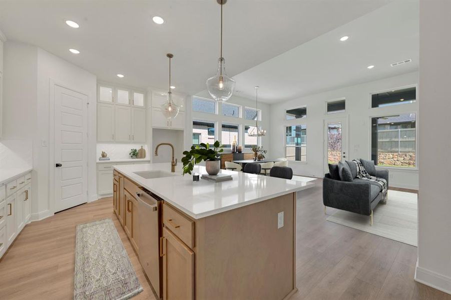 Open-concept kitchen featuring a large central island with an undermount sink, pendant lighting, shaker-style cabinetry, and wood-finish flooring
