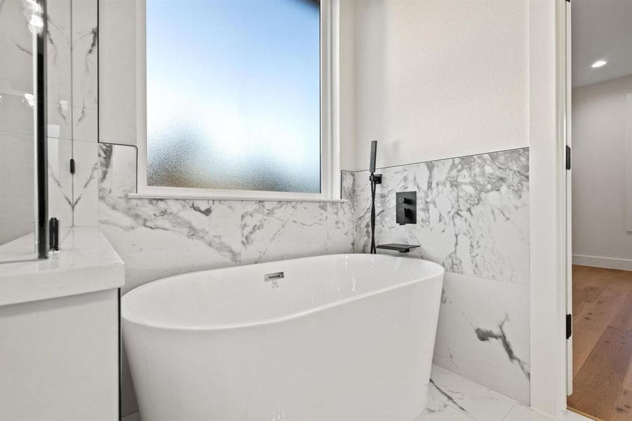 Bathroom with marble tiled floors, a freestanding bath, tile walls, vanity, and wainscoting