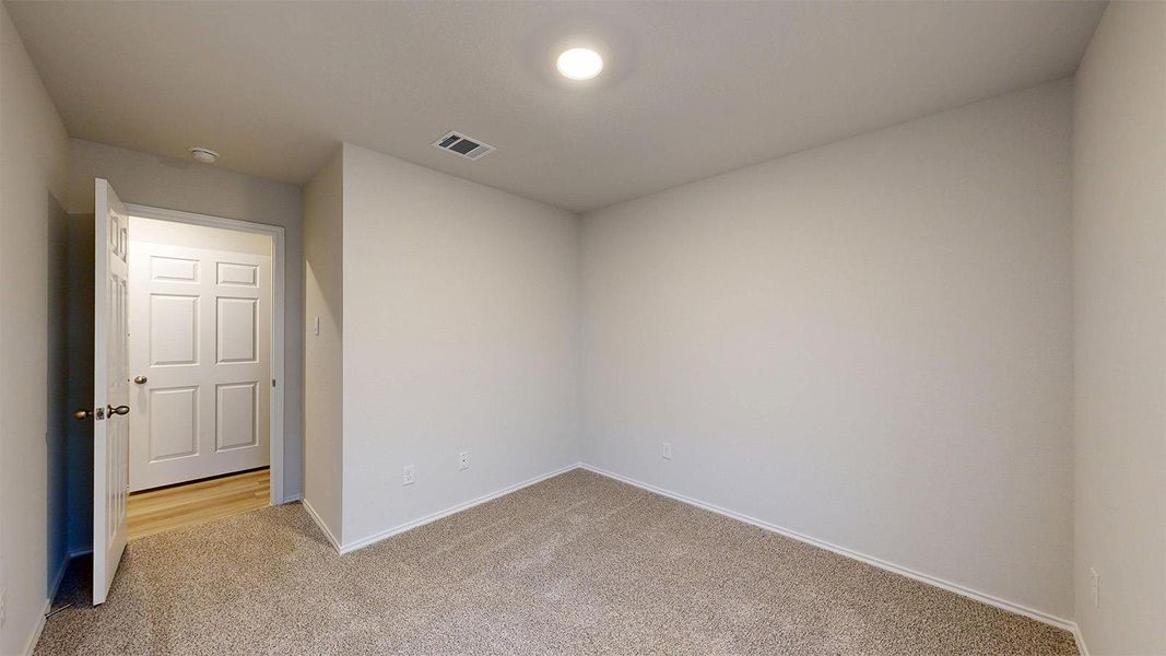 A well-lit, neutral-toned room features new carpet, an interior door, and clean baseboards.