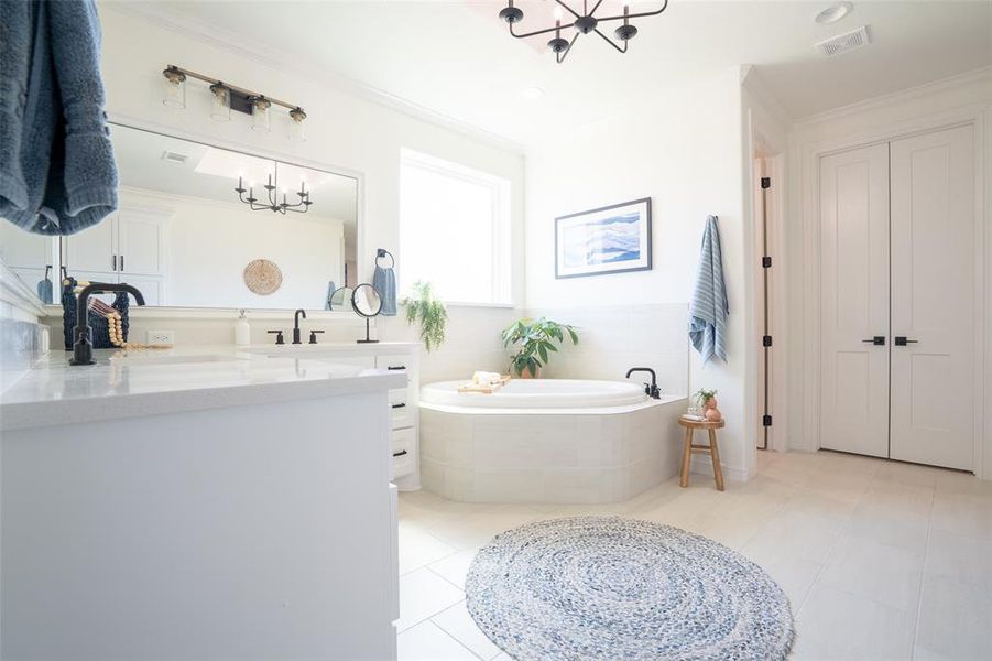 Bathroom featuring a chandelier, vanity, a garden tub, ornamental molding, and light tile patterned floors