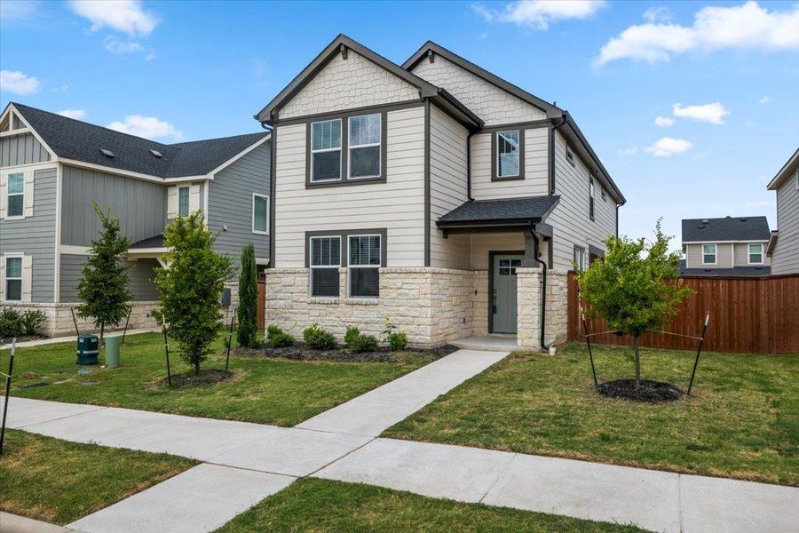 A charming two-story home presents a blend of stone and siding, complemented by manicured landscaping and a welcoming sidewalk.