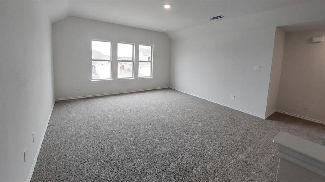 Carpeted empty room featuring vaulted ceiling and baseboards Carpeted empty room featuring vaulted ceiling and baseboards