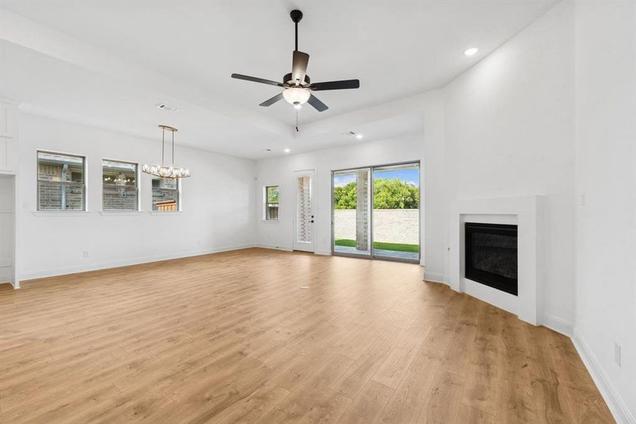 Unfurnished living room featuring ceiling fan, light wood finished floors, a glass covered fireplace, and hanging lights Unfurnished living room featuring ceiling fan, light wood finished floors, a glass covered fireplace, and hanging lights