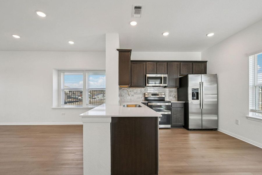 Kitchen with dark brown cabinetry, stainless steel appliances, light stone countertops, light wood-style flooring, and recessed lighting