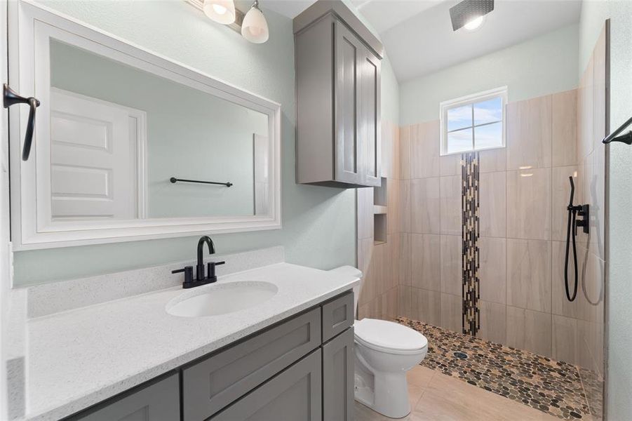 Bathroom featuring tile patterned floors, vanity, a tile shower, and toilet