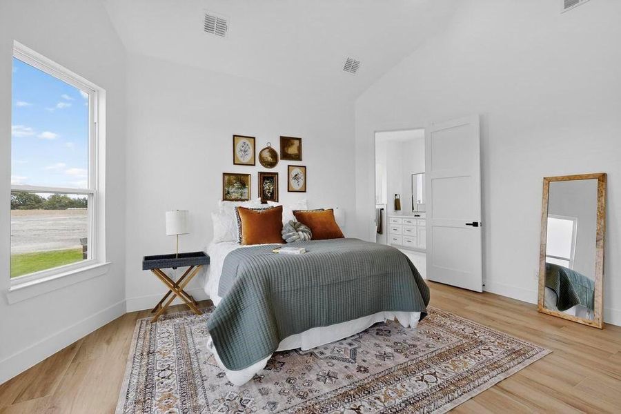 Bedroom featuring light wood-style flooring, ensuite bath, and high vaulted ceiling Bedroom featuring light wood-style flooring, ensuite bath, and high vaulted ceiling