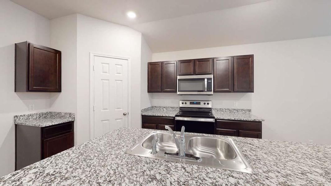Kitchen featuring a double stainless steel sink, a stainless steel microwave, a black electric range, dark wood-finish cabinetry, and speckled countertops