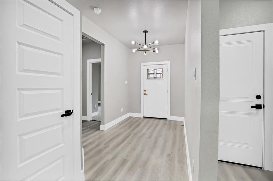 Entryway with light wood-type flooring and an inviting chandelier