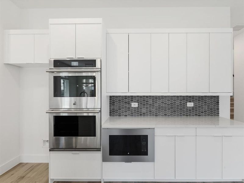 Kitchen with stainless steel appliances, white cabinets, modern cabinets, light stone counters, and light wood finished floors