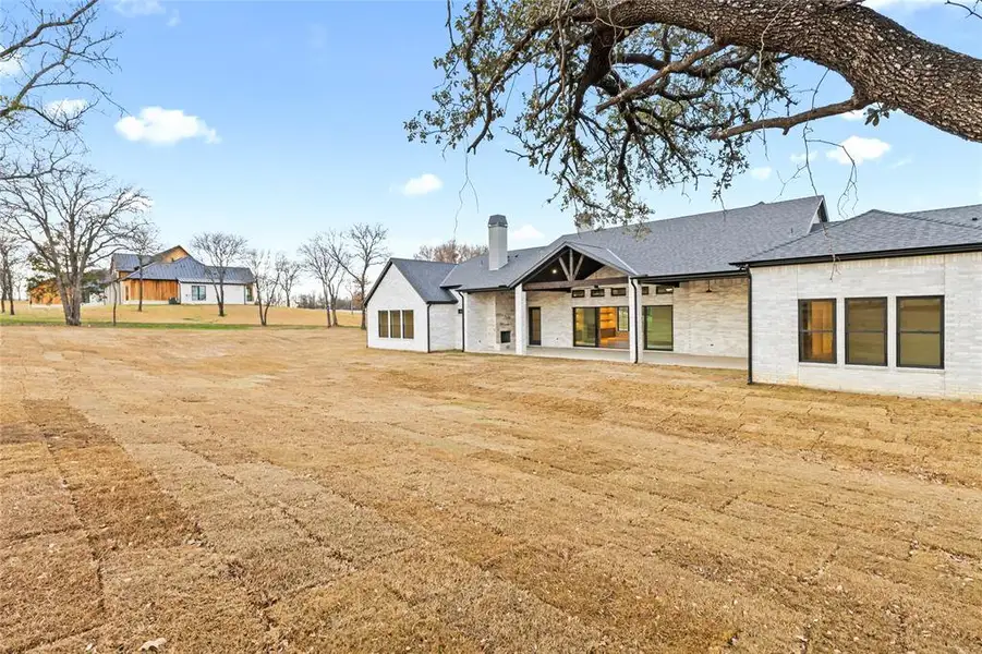 Spacious backyard with a covered patio featuring a vaulted ceiling and exposed beams, a large sliding glass door, and a stone exterior