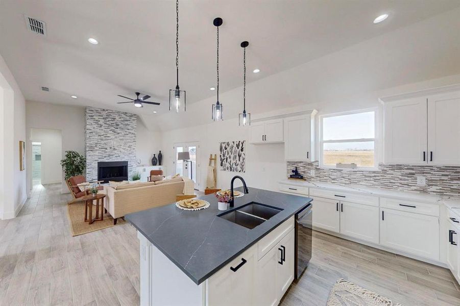 Kitchen with sink, vaulted ceiling, light wood-type flooring, an island with sink, and white cabinetry