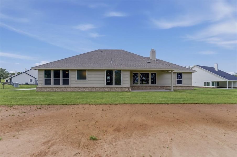 Rear exterior featuring a covered patio, multiple large windows, light-colored siding, and a stone foundation accent