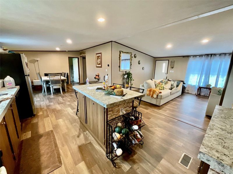 Open-concept living space featuring wood-finish flooring, recessed lighting, a kitchen island with stone accent paneling, and granite-look countertops