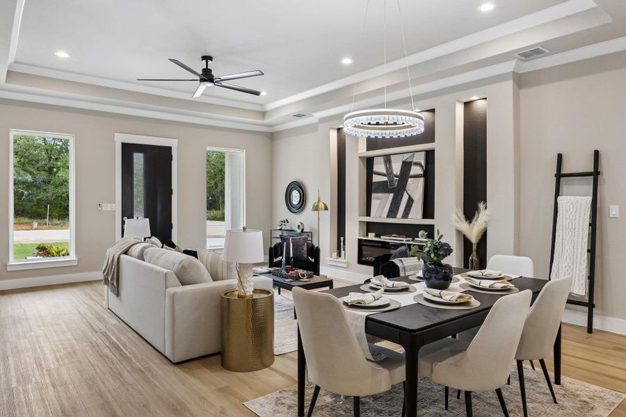 Natural light floods this inviting living and dining space with elegant tray ceilings and rich wood flooring.