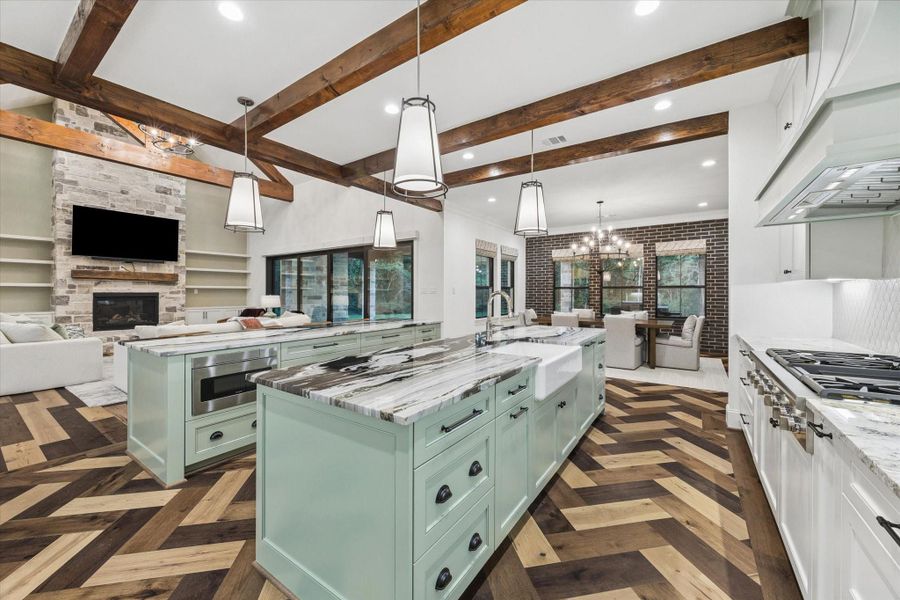 The oversized gathering island provides generous seating and serves as the social heart of this exceptional chef’s kitchen. Fantasy Zebra marble introduces dramatic natural movement, while custom sage-green cabinetry and rich wood ceiling beams add warmth and character. The kitchen also features paneled appliance integration, two refrigerators with freezers, two dishwashers, double ovens, a warming drawer, built-in microwave, and an impressive six-burner Thermador cooktop with integrated griddle.