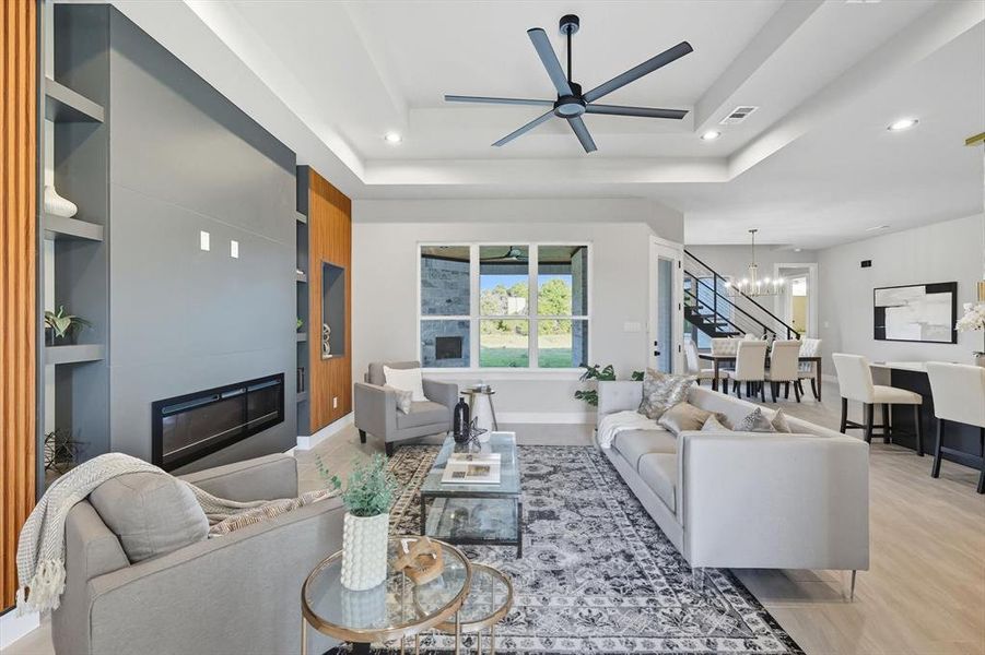 Living room with a tray ceiling, a large fireplace, a chandelier, recessed lighting, and a ceiling fan Living room with a tray ceiling, a large fireplace, a chandelier, recessed lighting, and a ceiling fan