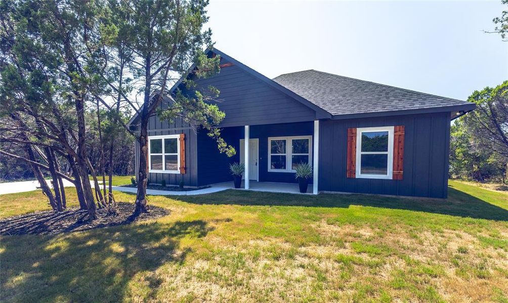 View of front of home featuring board and batten siding, a front yard, a shingled roof, and a patio area View of front of home featuring board and batten siding, a front yard, a shingled roof, and a patio area