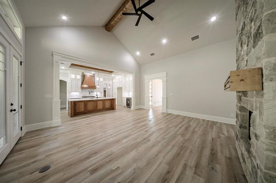 Unfurnished living room with beamed ceiling, light wood-style floors, a stone fireplace, high vaulted ceiling, and recessed lighting Unfurnished living room with beamed ceiling, light wood-style floors, a stone fireplace, high vaulted ceiling, and recessed lighting