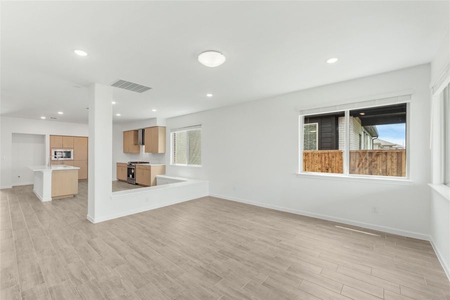 Open living area with light wood floors flowing into kitchen with light wood cabinets and stainless appliances