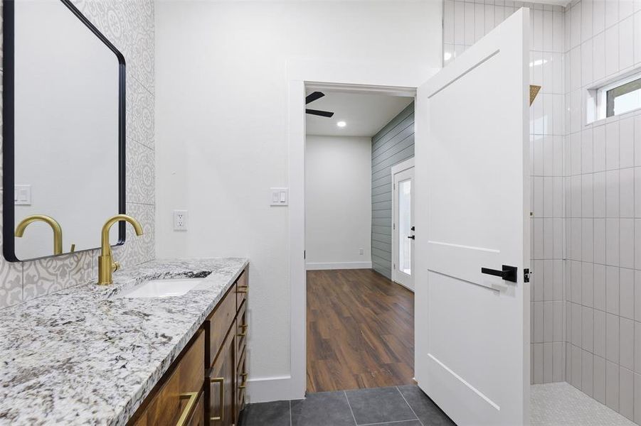 Bathroom vanity featuring a light-toned countertop, under-mount sink, and brass-finish faucet Bathroom vanity featuring a light-toned countertop, under-mount sink, and brass-finish faucet