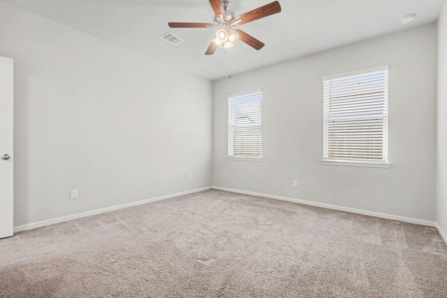 Primary bedroom with soft carpet, ceiling fan, and natural light from dual windows. Primary bedroom with soft carpet, ceiling fan, and natural light from dual windows.