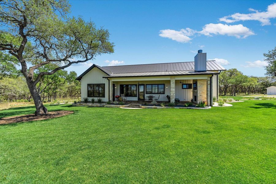 Rear view of house with a porch, a chimney, a lawn, a standing seam roof, and board and batten siding