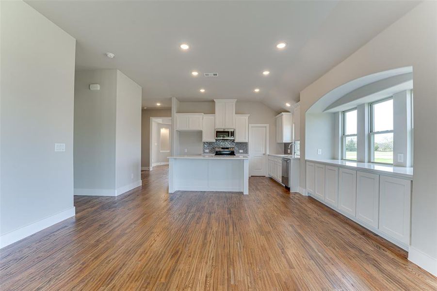 Kitchen with stainless steel appliances, sink, hardwood / wood-style floors, white cabinetry, and lofted ceiling