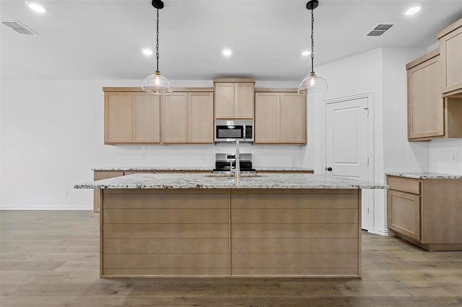 Kitchen with light brown cabinetry, light hardwood / wood-style flooring, and appliances with stainless steel finishes