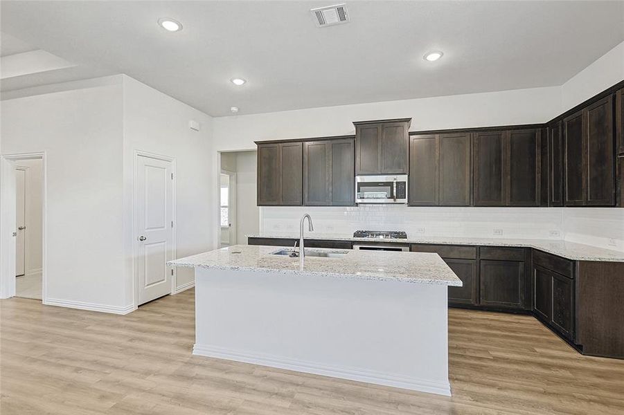 Kitchen featuring a kitchen island with sink, sink, stainless steel appliances, and light hardwood / wood-style flooring