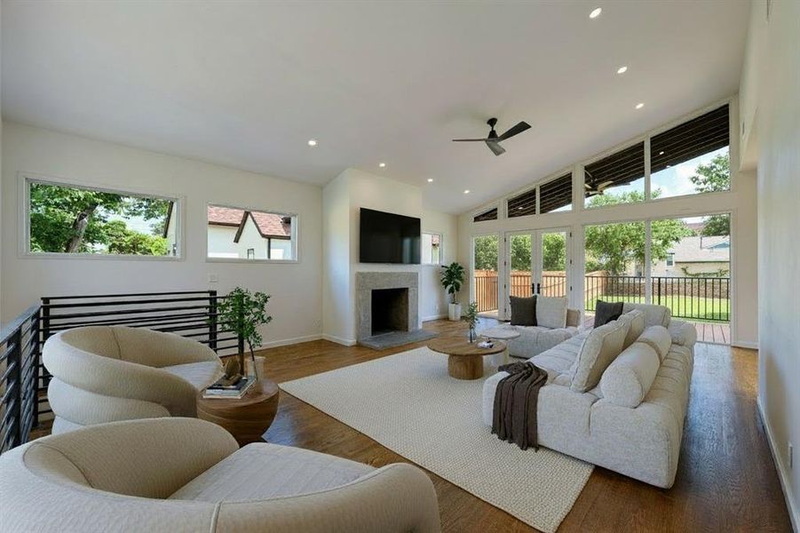 Living area with wood finished floors, recessed lighting, a fireplace with raised hearth, a high ceiling, and a ceiling fan